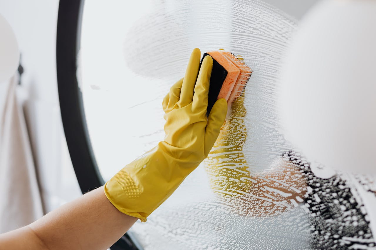 who-we-are-03 Anonymous person in yellow rubber gloves using simple sponge for cleaning mirror in bathroom